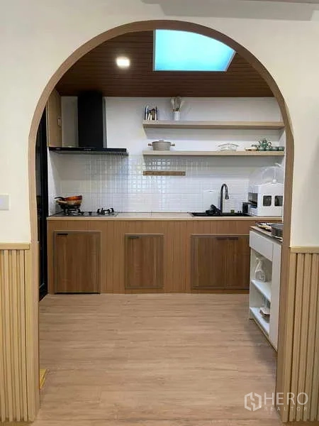 Townhouse for rent or sale in Bang Kapi, Bangkok - Archway framing a modern kitchen with wood cabinets, white tiles and skylight.