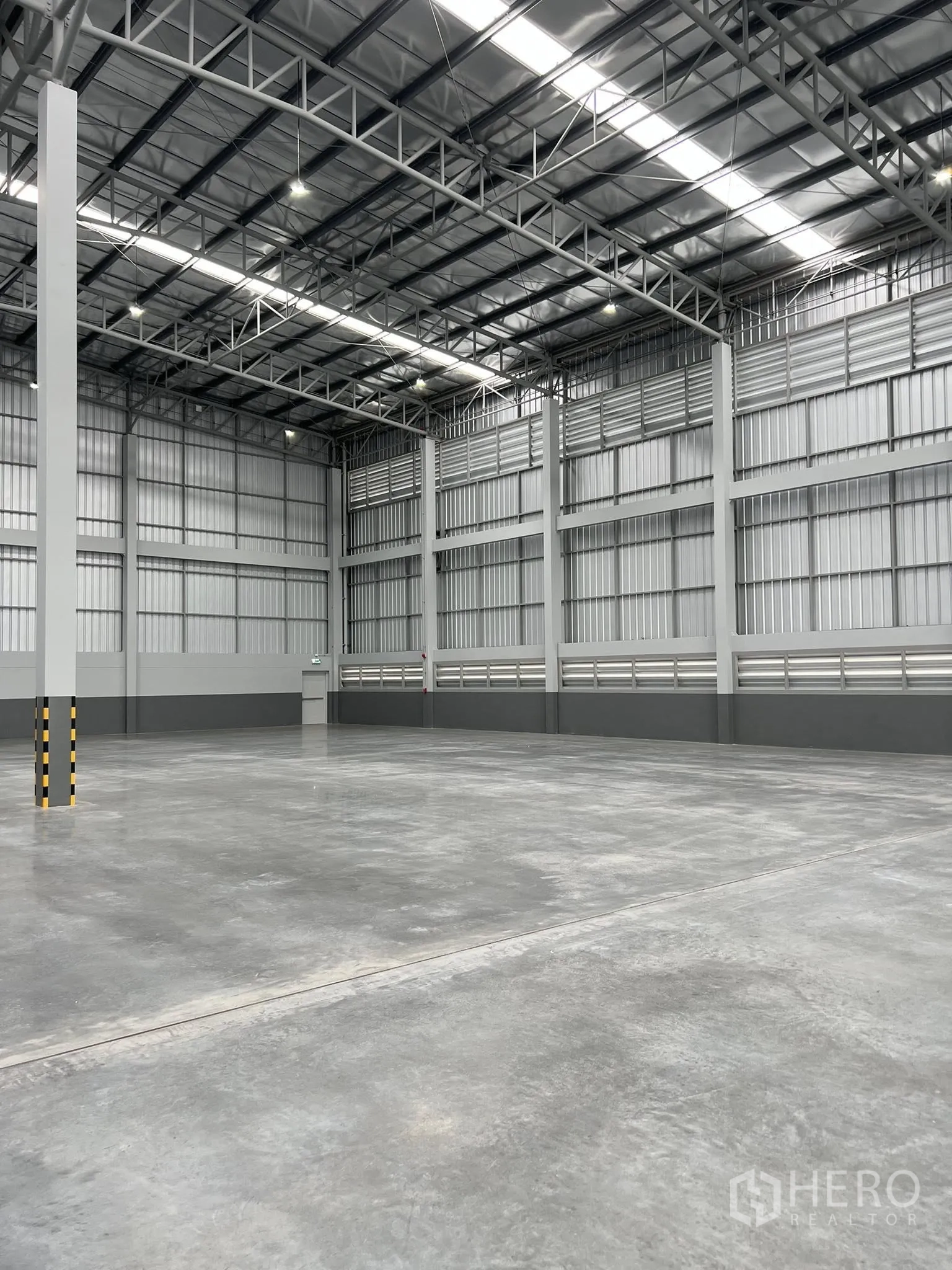 Warehouse for rent in Phra Pradaeng, Samut Prakan - Open storage area showing tall walls, support columns, and roof skylight strips.