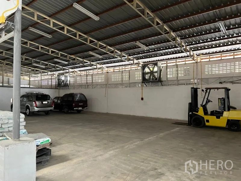 Warehouse for rent in Suan Luang, Bangkok - Wide parking and staging zone with industrial wall fans and a forklift under a ventilated metal roof.