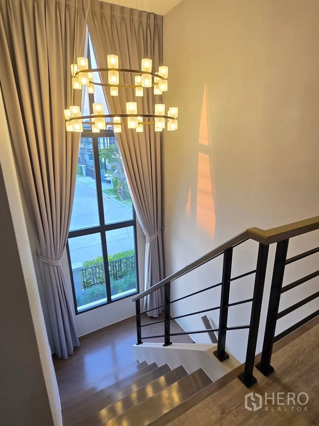 Detached House for rent or sale in Bang Phli, Samut Prakan - Staircase with modern black railing, tall window, and statement double-ring chandelier.