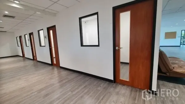 Office Space for rent in Watthana, Bangkok - Hallway view of multiple office doors and interior windows with wood accents and vinyl flooring.