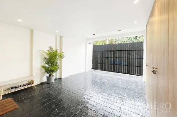 联排别墅 出租在Khlong Toei, Bangkok - 带顶车位，黑色地砖、绿植、长凳与金属大门。