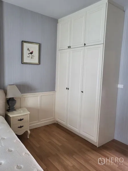 Townhouse for rent in Wang Thonglang, Bangkok - Corner of bedroom with tall white wardrobe, nightstand and framed art.