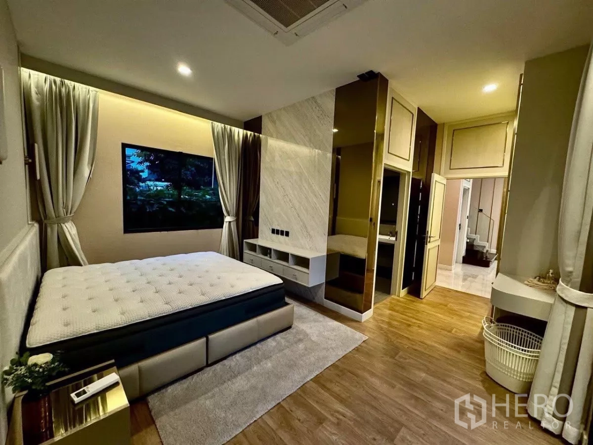 Detached House for sale in Saphan Sung, Bangkok - Cozy bedroom with TV wall, ensuite access and warm wood flooring.