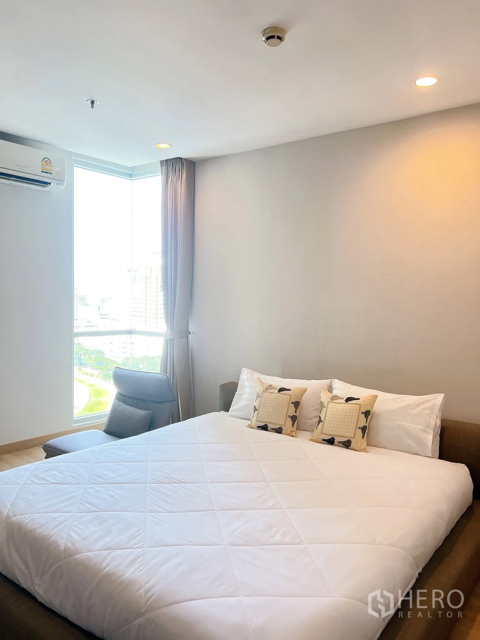 คอนโด for rent in Pathum Wan, Bangkok - ห้องนอนเตียงใหญ่ เก้าอี้นั่งมุมห้อง และวิวเมืองผ่านหน้าต่างสูง