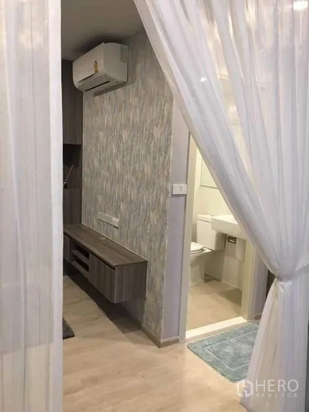 คอนโด ขายในBang Na, Bangkok - มุมมองจากห้องนั่งเล่นสู่ห้องนอนและห้องน้ำ มีผ้าม่านโปร่ง โต๊ะวางทีวีบิลท์อิน และเครื่องปรับอากาศ