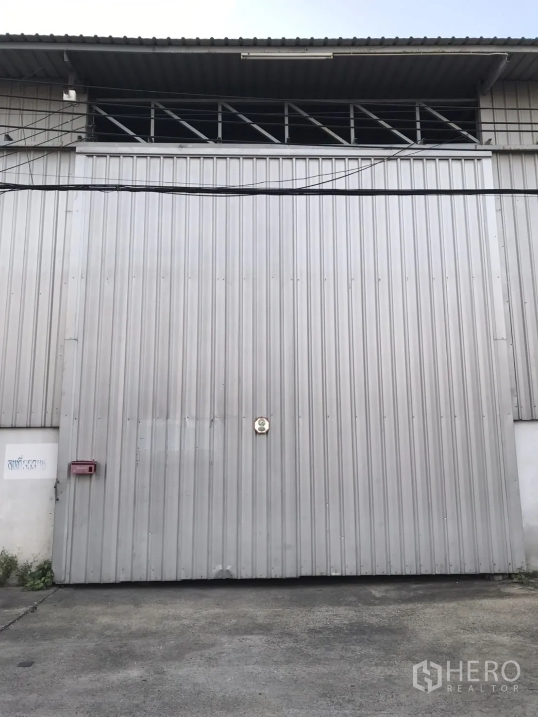 Warehouse for rent in Phra Pradaeng, Samut Prakan - Tall sliding metal warehouse door with ventilation panels above and a concrete apron in front.