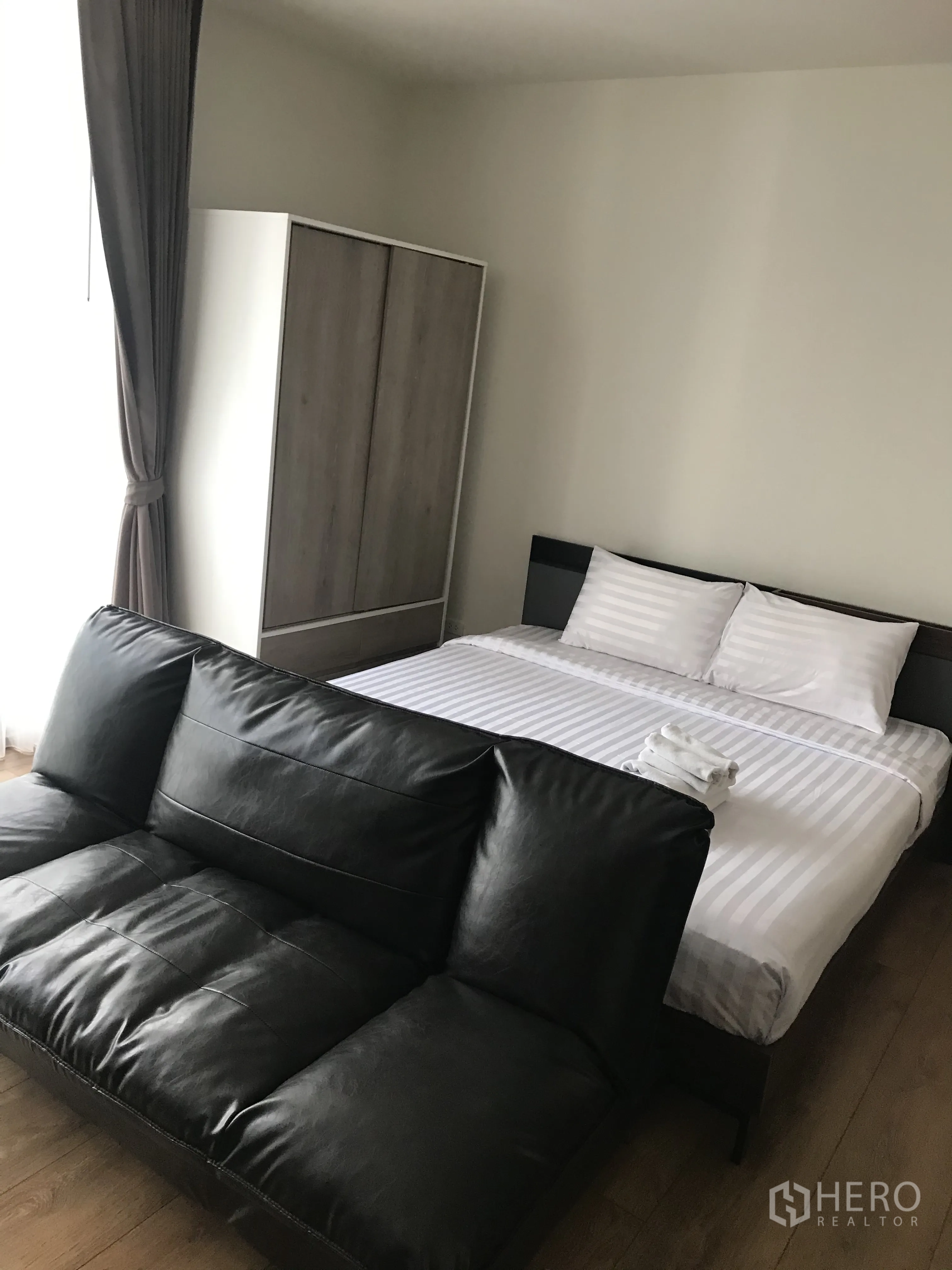 Condominium for sale in Khlong Toei, Bangkok - Bedroom with bed, wardrobe, and dark leather sofa by the window.