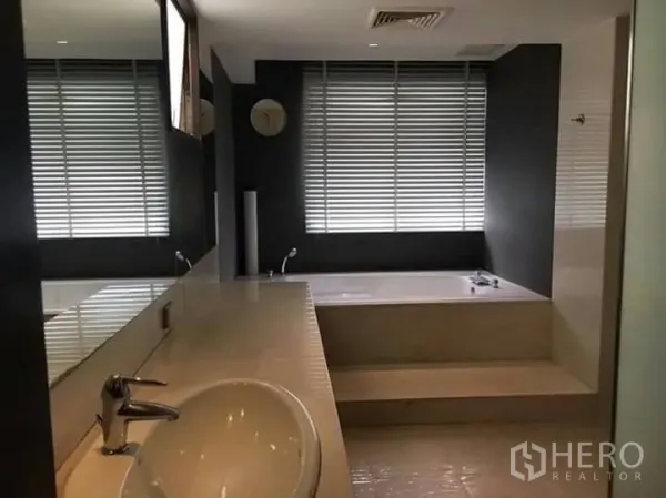 Condominium for rent in Watthana, Bangkok - Modern bathroom featuring a long vanity with mirror, window blinds, and a raised soaking bathtub.