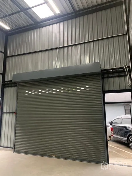 Warehouse for rent in Bangkok - High-ceiling warehouse interior with metal cladding and a motorized rolling shutter door.