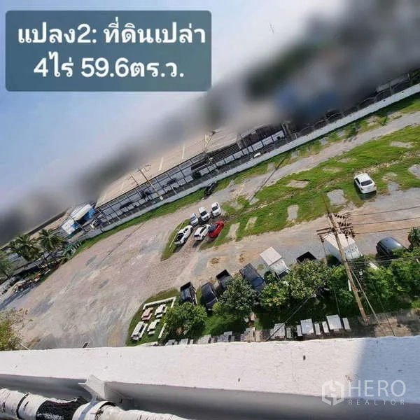 Land for rent in Krathum Baen, Samut Sakhon - Aerial view of a large vacant plot with gravel and grass, boundary wall, utility poles and parked cars in an industrial area.