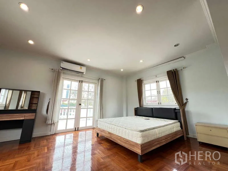Detached House for rent in Bang Phli, Samut Prakan - Sunlit upstairs bedroom with parquet floor, AC, and French balcony doors.