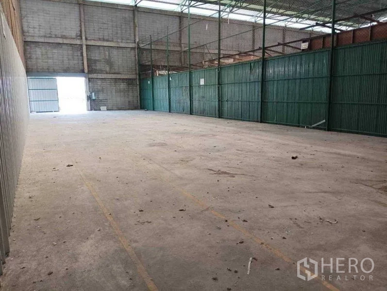 Warehouse for rent in Prawet, Bangkok - Open-plan storage area with skylight roof panels and green metal side partitions.