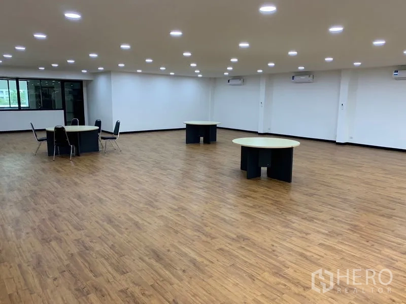 Office Space for rent in Khlong Toei, Bangkok - Large open workspace with wood flooring, round tables, recessed lighting and wall-mounted air conditioners.