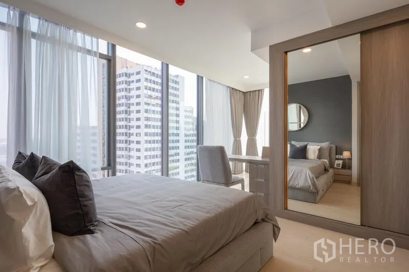Condominium for rent in Khlong Toei, Bangkok - Master bedroom featuring mirrored wardrobe, large windows, and urban views.