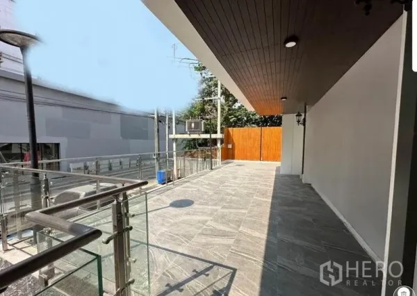 พื้นที่ขายปลีก ให้เช่า - พื้นที่ลานมุมอาคารพร้อมราวกระจก รั้วไม้ และพื้นกระเบื้องหินสีเทา เหมาะสำหรับจัดแสดงหรือที่นั่ง