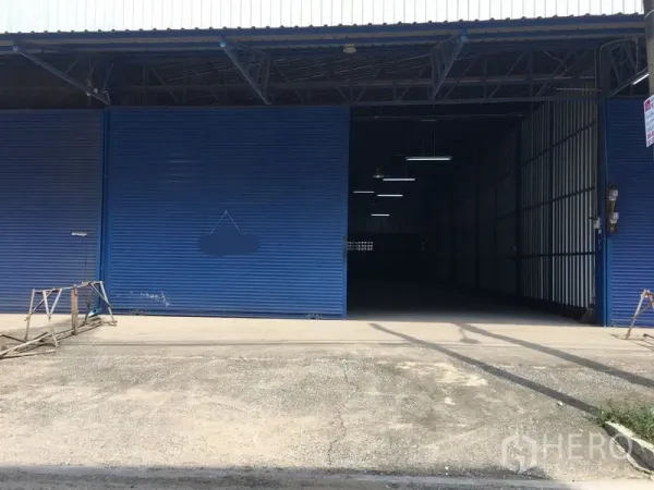 คลังสินค้า ให้เช่าในBang Kapi, Bangkok - ด้านหน้าโกดัง ประตูม้วนสีน้ำเงินขนาดใหญ่ พร้อมลานคอนกรีตสำหรับจอดและขนถ่ายสินค้า