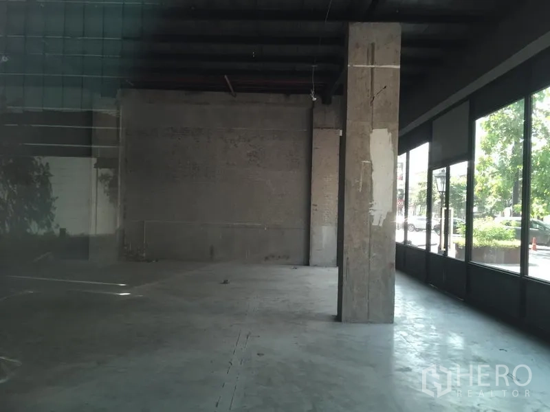 Retail Space for rent in Khlong Toei, Bangkok - Spacious shop space with a central column and wide street-facing glass frontage with greenery outside.