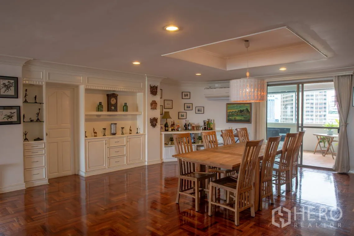 Apartment for rent in Khlong Toei, Bangkok - Dining room with long wooden table, built-in cabinets, and balcony access.