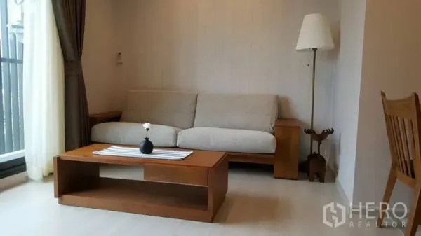 คอนโด ให้เช่าในKhlong Toei, Bangkok - ห้องนั่งเล่นสว่าง โซฟาผ้าสีอ่อน โต๊ะกาแฟไม้ และโคมไฟข้างประตูกระจกติดระเบียง