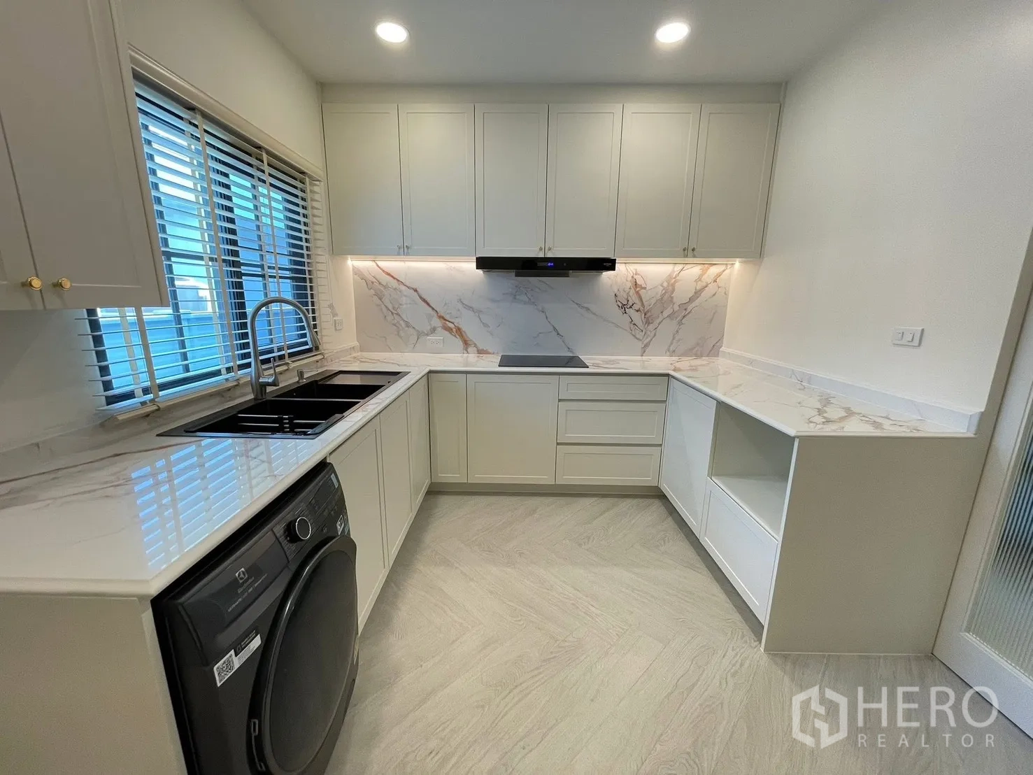 Detached House for rent in Bang Phli, Samut Prakan - Sleek L-shaped kitchen with marble-look counters and backsplash, induction hob, hood, double sink, and washer.