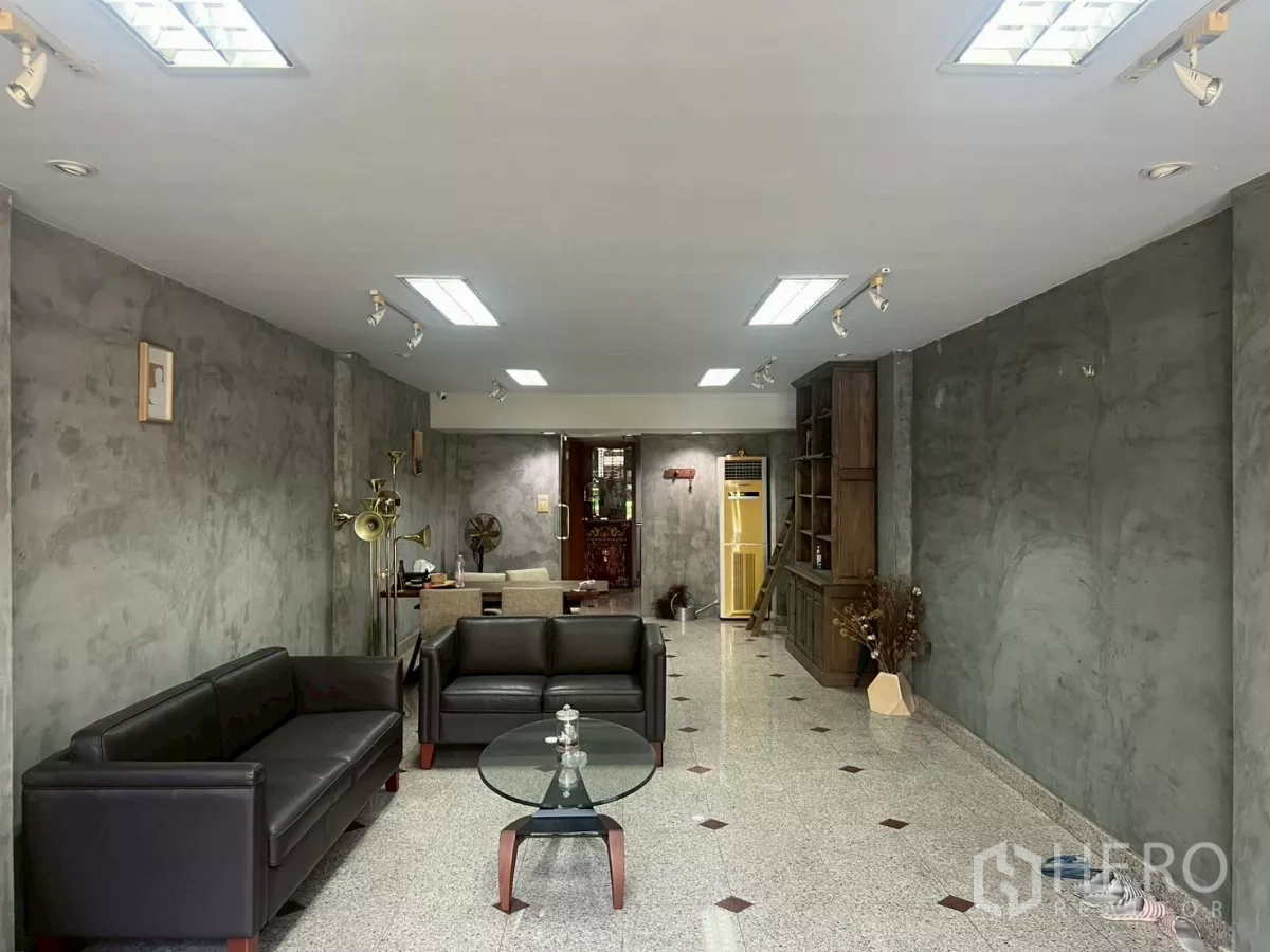 店屋 出租在Bang Rak, Bangkok - 一层展厅，花岗岩地面、灰色清水墙、沙发与射灯。