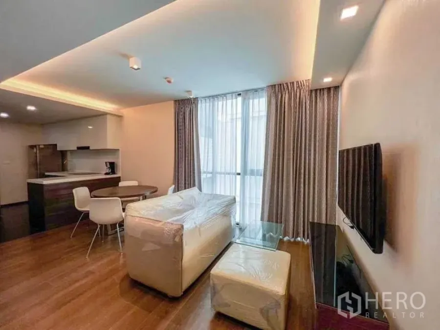 Condominium for sale in Huai Khwang, Bangkok - Living area with sofa set, TV, floor-to-ceiling curtains and a dining table beside the kitchen.