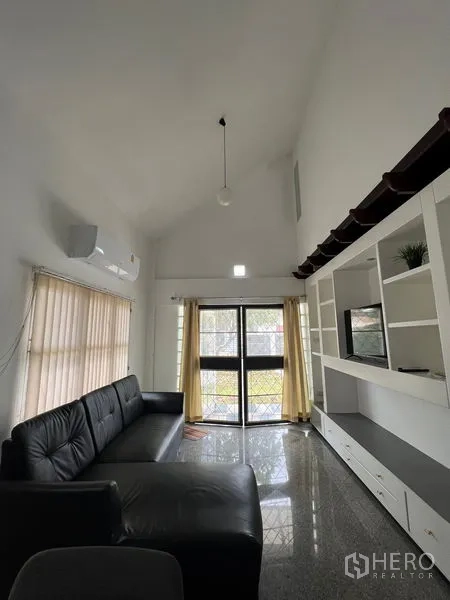 Detached House for rent in Saphan Sung, Bangkok - High-ceiling living room with black leather sofa, built-in media wall and sliding glass doors.