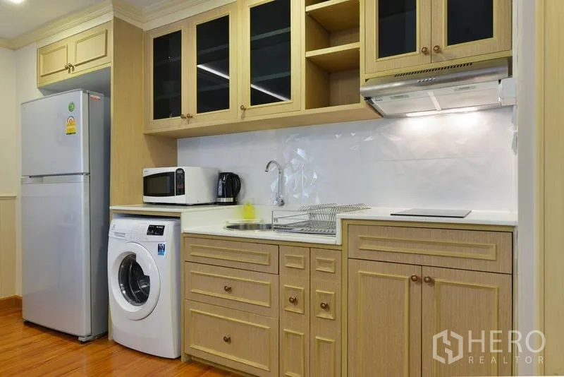 Apartment for rent in Khlong Toei, Bangkok - Compact kitchen with wood cabinets, sink, cooktop, hood, microwave, fridge and washer.