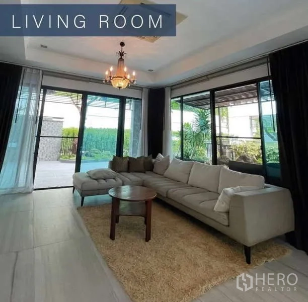 独立式住宅 出售在Khlong Toei, Bangkok - 客厅配L型沙发、吊灯与推拉落地门通向露台。