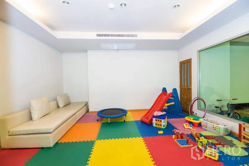 房间 出租在Sathon, Bangkok - 室内儿童游乐室，彩色地垫、滑梯与玩具及沙发座位。