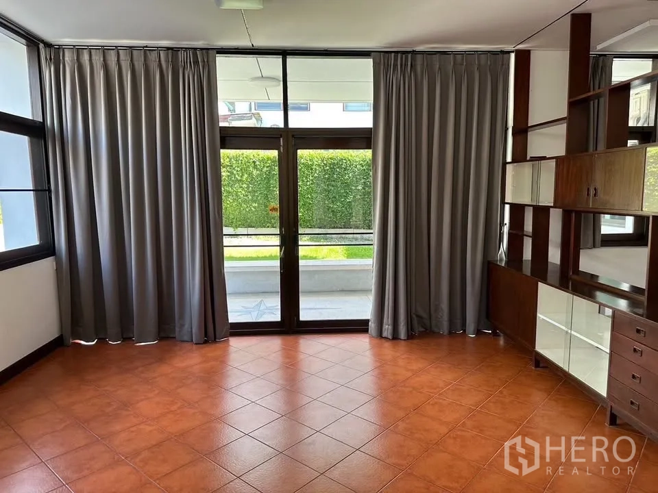 独栋房屋 for rent in Phra Khanong, Bangkok - 客厅明亮，赤陶色地砖，落地玻璃门、窗帘与内置置物架。
