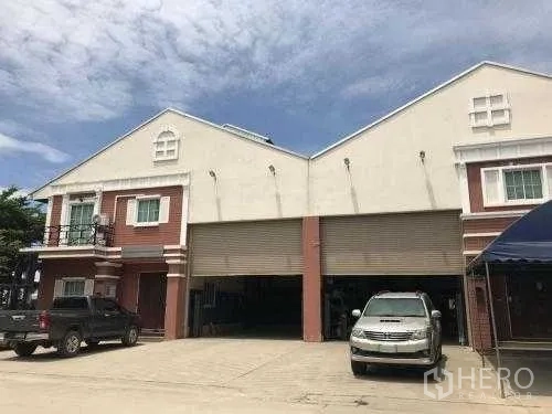 货栈 出租在Samut Sakhon - 双开间仓库立面，高卷帘门与停车区。