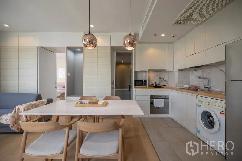 Condominium for rent in Watthana, Bangkok - Dining table for four under copper pendant lights facing an L-shaped kitchen.