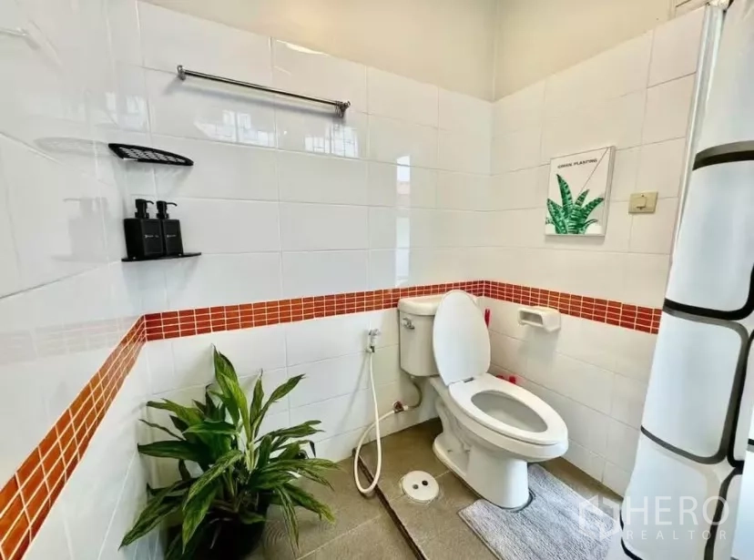Townhouse for rent in Watthana, Bangkok - Clean bathroom with white tiles and orange accent strip, toilet and shower area with curtain.
