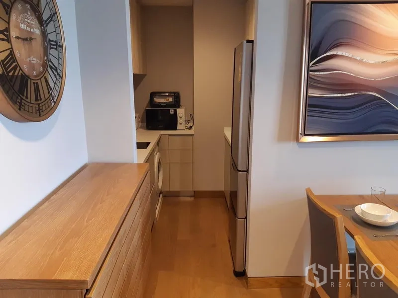 Condominium for rent in Khlong Toei, Bangkok - Hallway leading to the fitted kitchen beside the dining table, wall clock and abstract artwork.