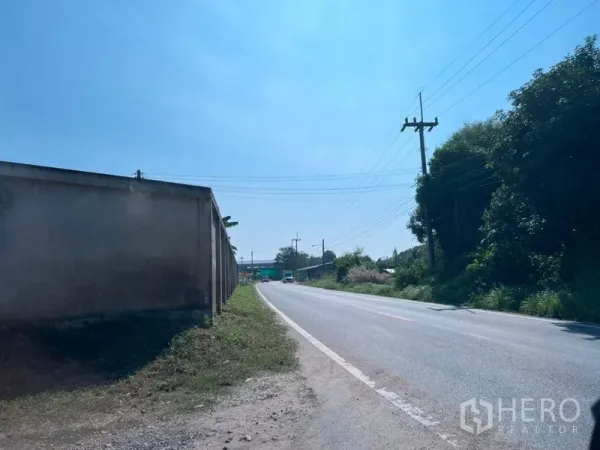 โรงงาน ขายในPhanat Nikhom, Chon Buri - ถนนทางเข้าปูยางข้างกำแพงที่ดิน มีเสาไฟและต้นไม้สองข้างทาง.