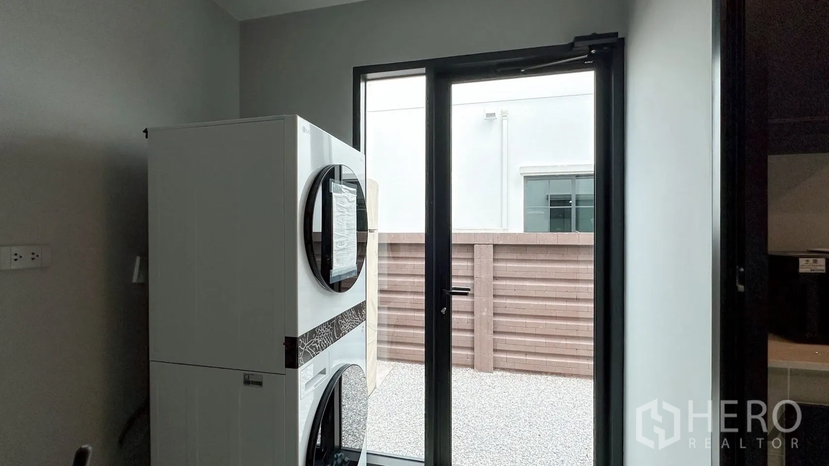 Detached House for rent in Bang Phli, Samut Prakan - Laundry room with stacked washer–dryer and a glass door opening to a pebble side yard.