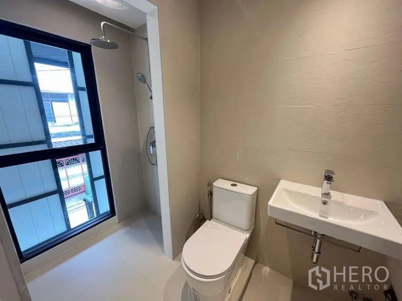 Townhouse for sale in Khlong Toei, Bangkok - Bathroom with large window, rain shower, toilet and wall-mounted sink.