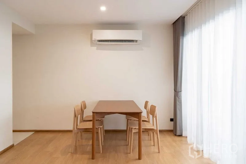 Condominium for rent in Phra Khanong, Bangkok - Dining area with wooden table and four chairs beside a large curtained window.