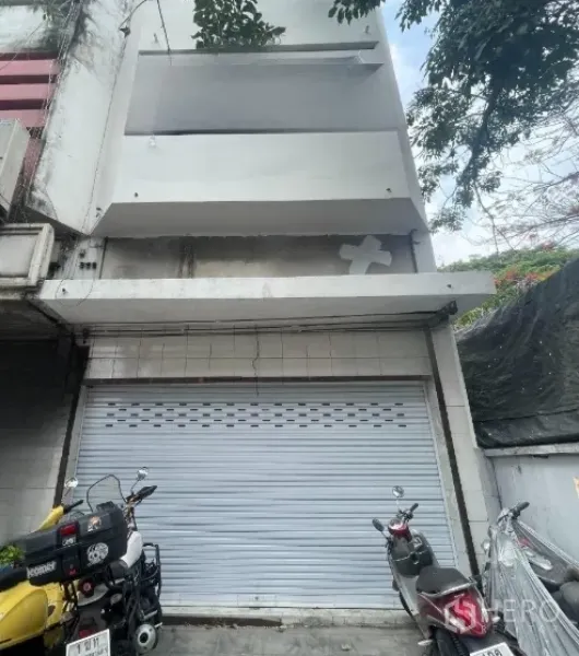 อาคารพาณิชย์ ให้เช่าในWatthana, Bangkok - ด้านหน้าตึกแถวสีขาวหลายชั้น ประตูลูกกรงม้วนปิด มีรถมอเตอร์ไซค์จอดหน้าอาคาร