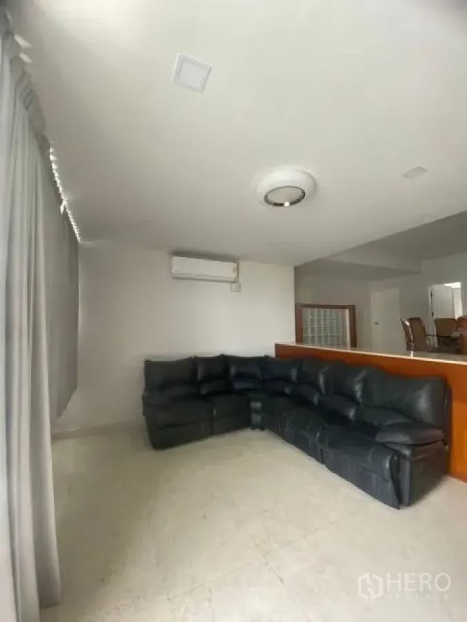 公寓 出租在Sathon, Bangkok - 明亮客厅，黑色真皮转角沙发，瓷砖地面，空调与落地窗帘。