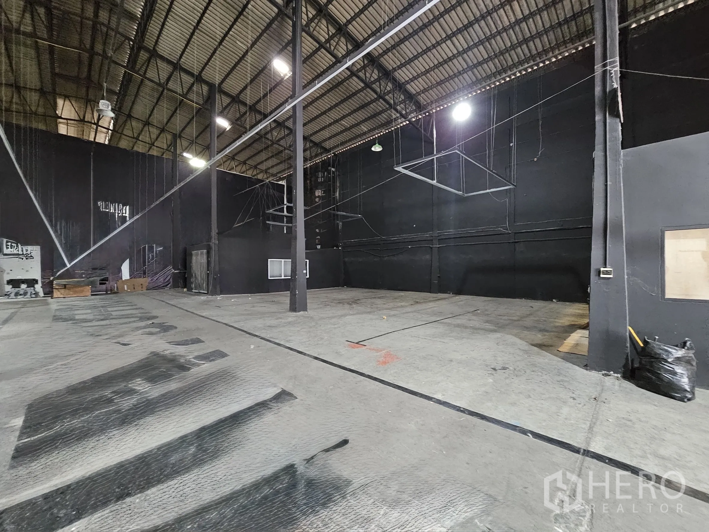 Warehouse for rent in Khlong Toei, Bangkok - Open storage area with central steel columns, overhead lighting, and partitioned rooms.