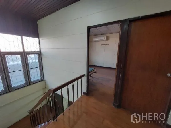 Townhouse for sale - Upper landing with wooden stairs, tall window, and a doorway leading to an air-conditioned bedroom.