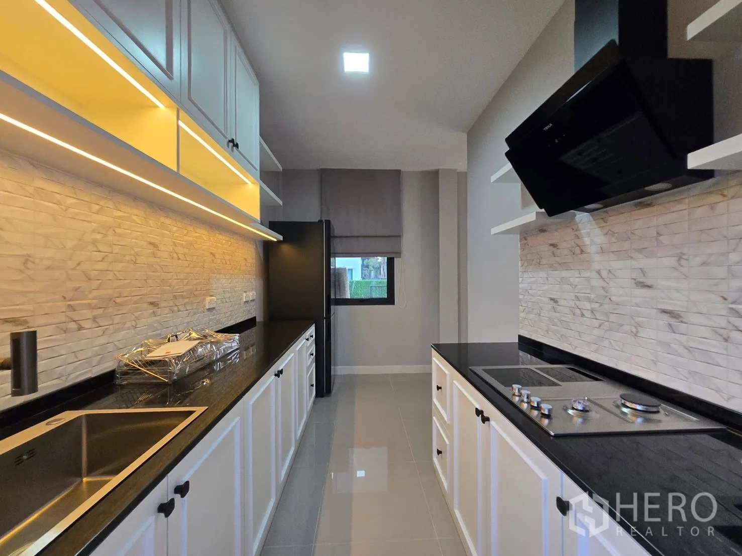 Detached House for rent or sale in Bang Phli, Samut Prakan - Galley kitchen with white shaker cabinets, black countertops, cooktop, and range hood.