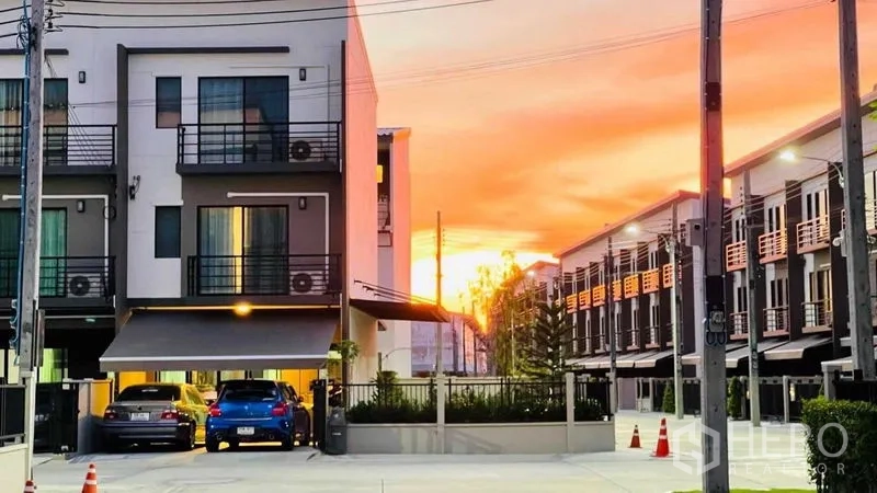 联排别墅 出租或出售在Prawet, Bangkok - 现代三层联排别墅社区外观，夕阳下带有车棚与门禁入口。