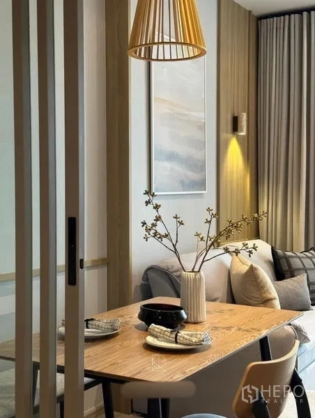 公寓 出租或出售在Watthana, Bangkok - 摆盘好的餐桌与木吊灯，旁边是沙发与墙面装饰画。