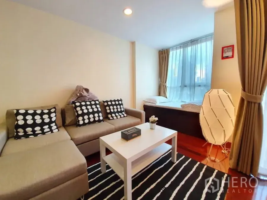 Condominium for rent or sale in Pathum Wan, Bangkok - Living area with L-shaped sofa, white coffee table and a daybed beside full-height windows.