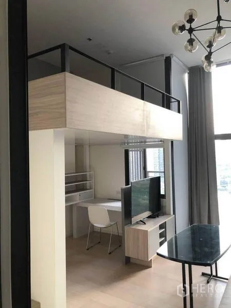 Condominium for sale in Ratchathewi, Bangkok - Open-plan living room with TV, study desk beneath mezzanine and a glass dining table.