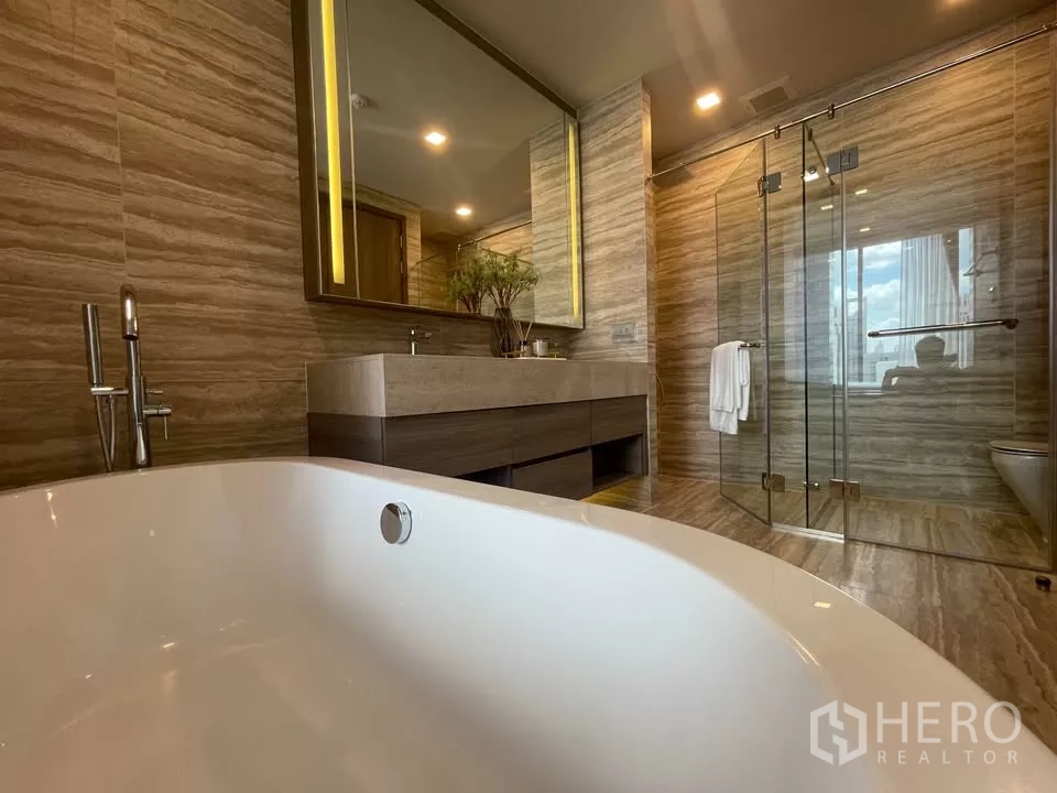 Condominium for rent in Watthana, Bangkok - Deep soaking bathtub facing the vanity and shower in stone-tiled bathroom.